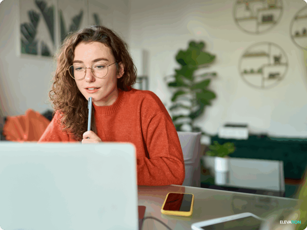Young female sitting at a laptop computer holding pen